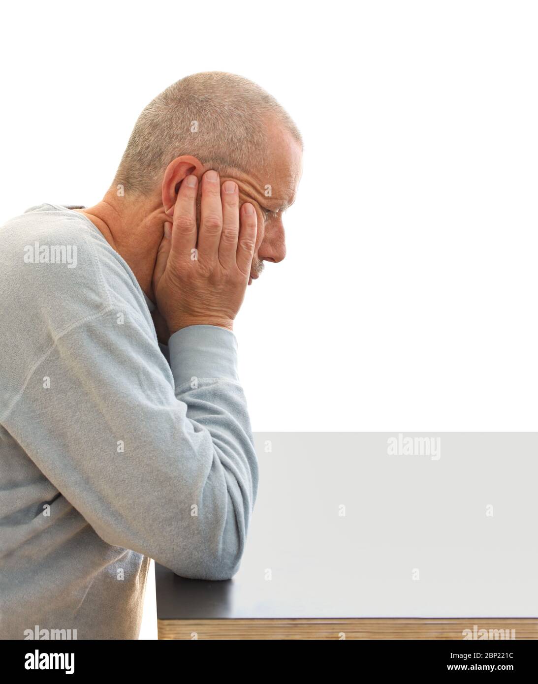 Thoughtful man with a depressed facial expression holds his head with his hands by a table. Close-up image isolated on white background. Stock Photo