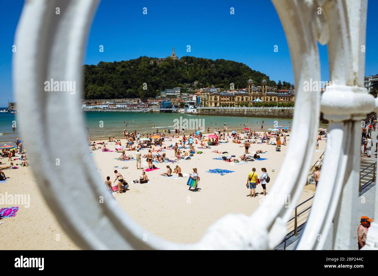 Donostia, Gipuzkoa, Basque Country, Spain - July 12th, 2019 : View through the iconic banister of La Concha beach. Sunbathers and Urgull hill in backg Stock Photo