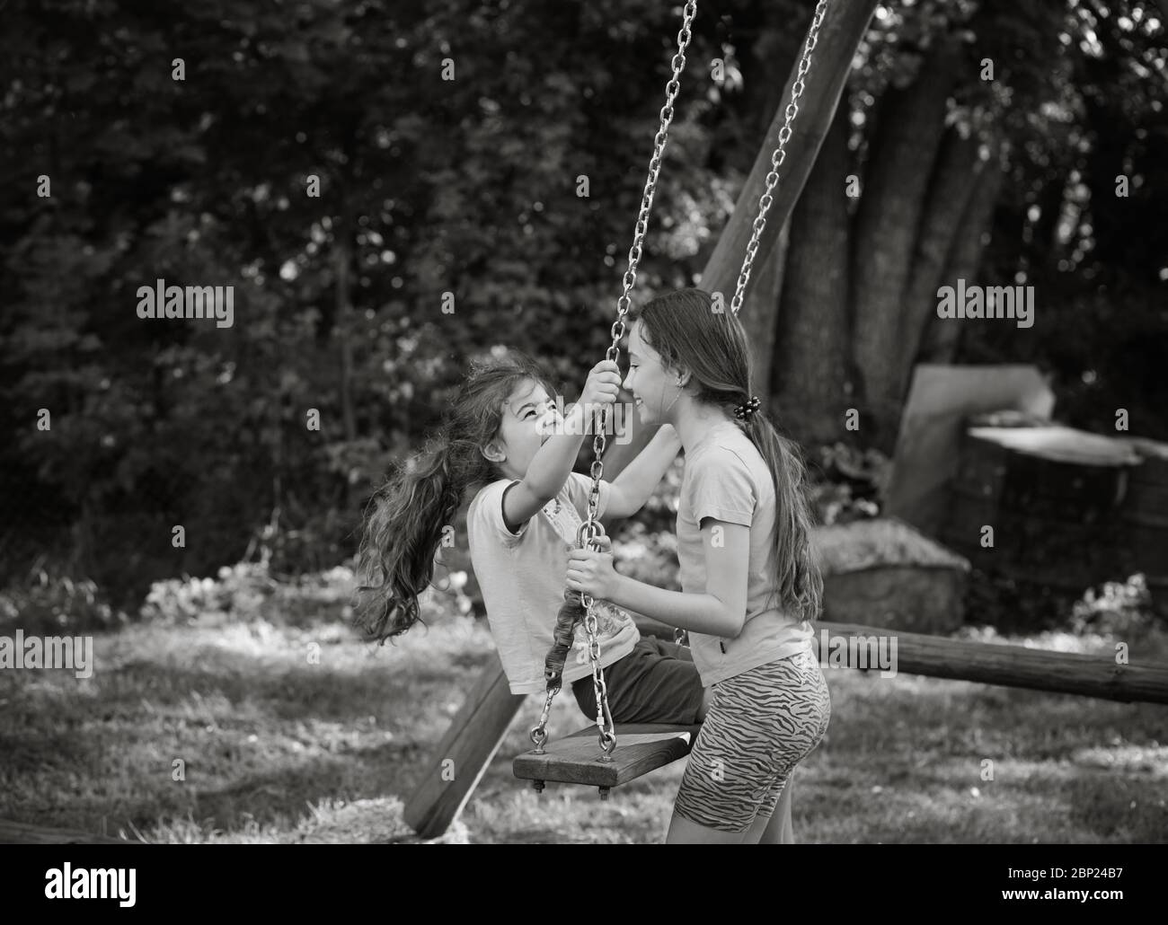 Two happy beautiful girls playing on swing and smiling at warm  summer day Stock Photo