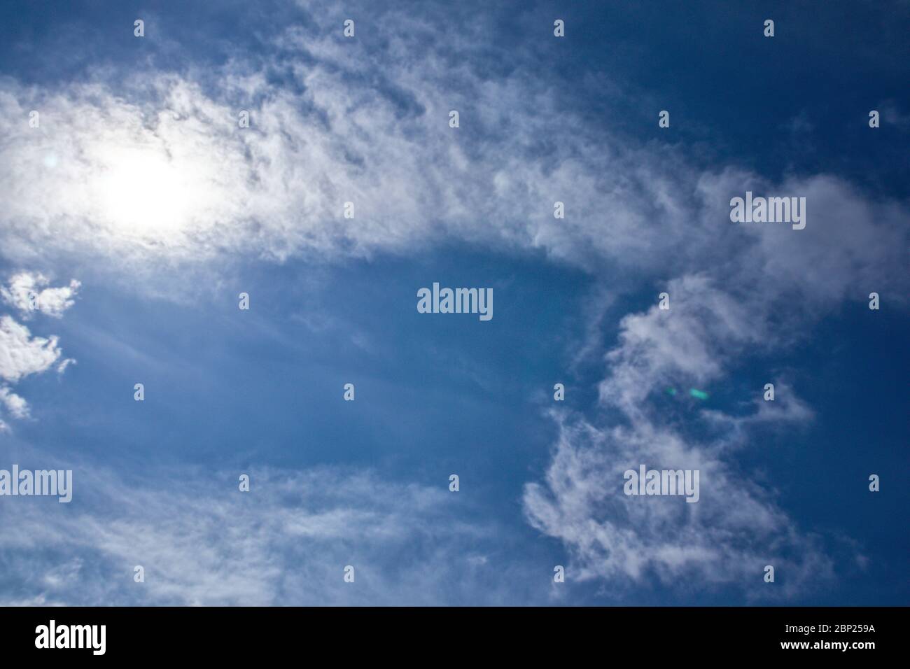 White clouds on the blue clean sky with sun rays.  Stock Photo