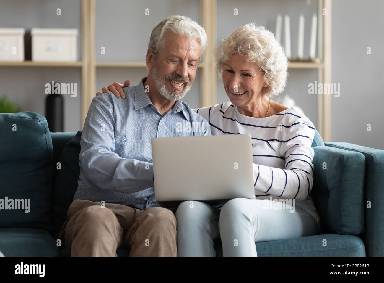 Happy older spouses sitting on sofa, looking at computer screen. Stock Photo