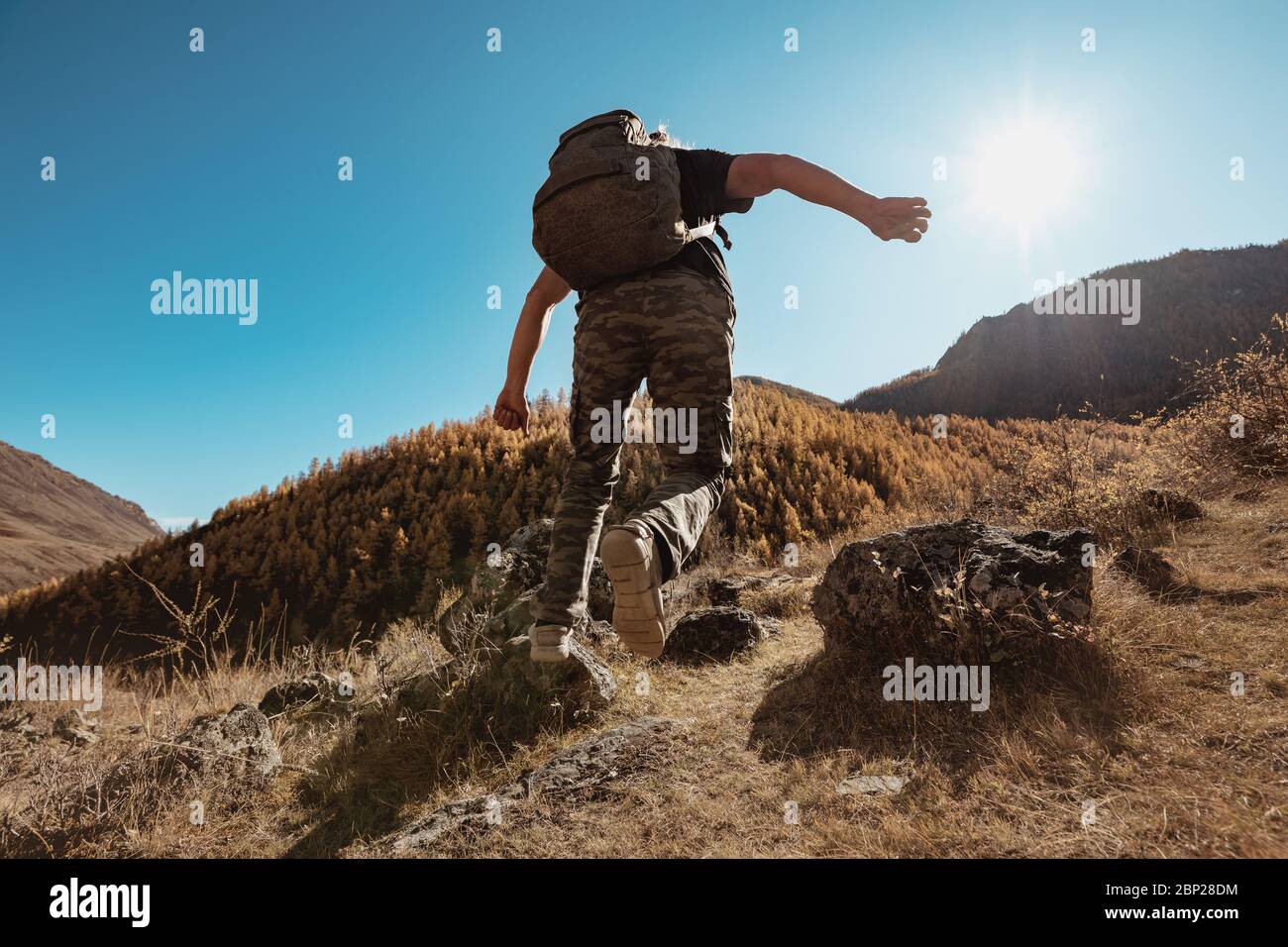 Active hiker with backpack runs and jums between rocks in mountains Stock Photo