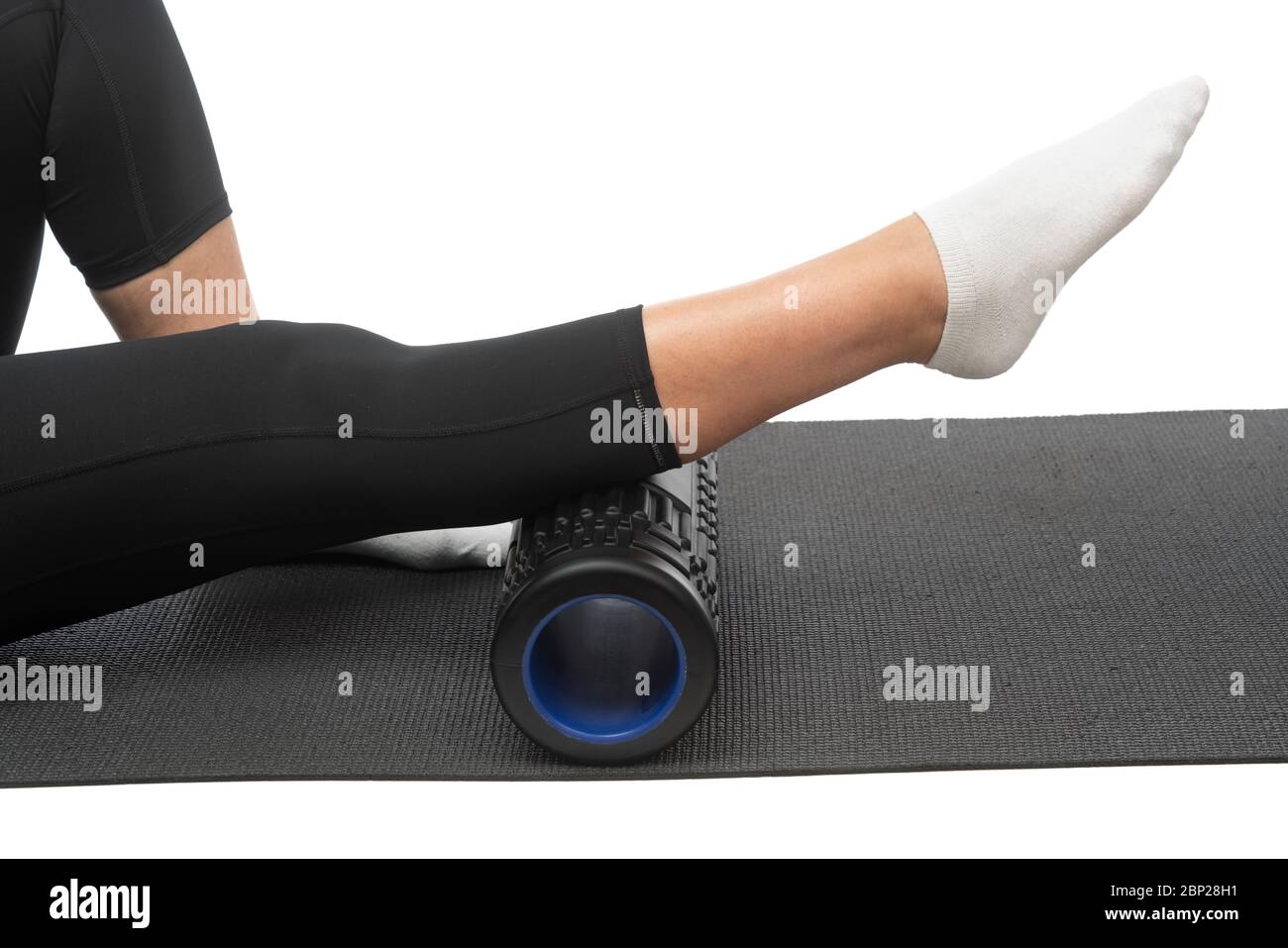 A middle-aged woman on a myofascial roller does a leg shin massage on a white background. Stock Photo