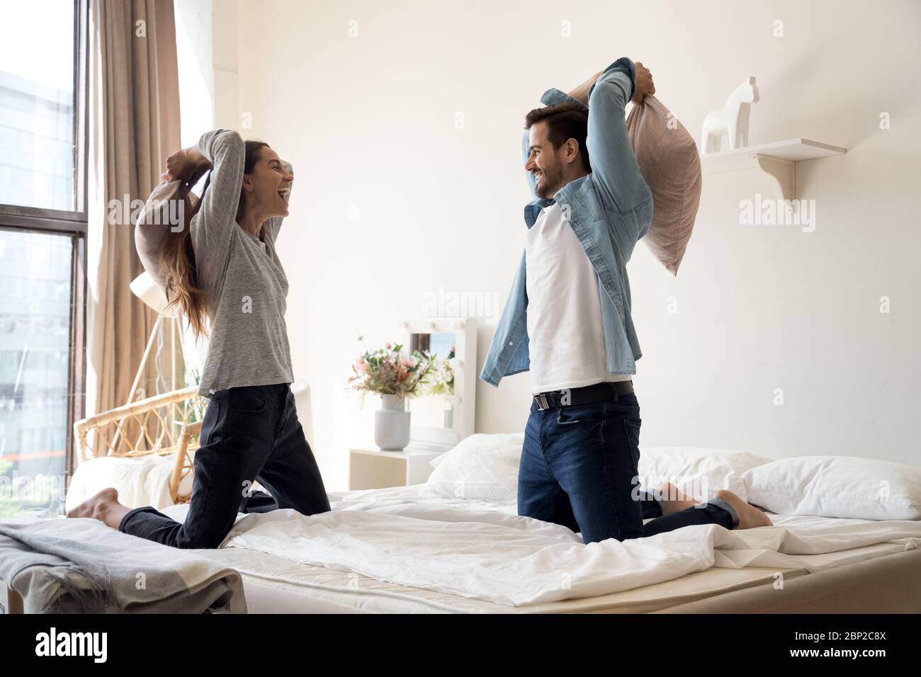 Overjoyed millennial couple have fun in pillow fight in bedroom Stock Photo