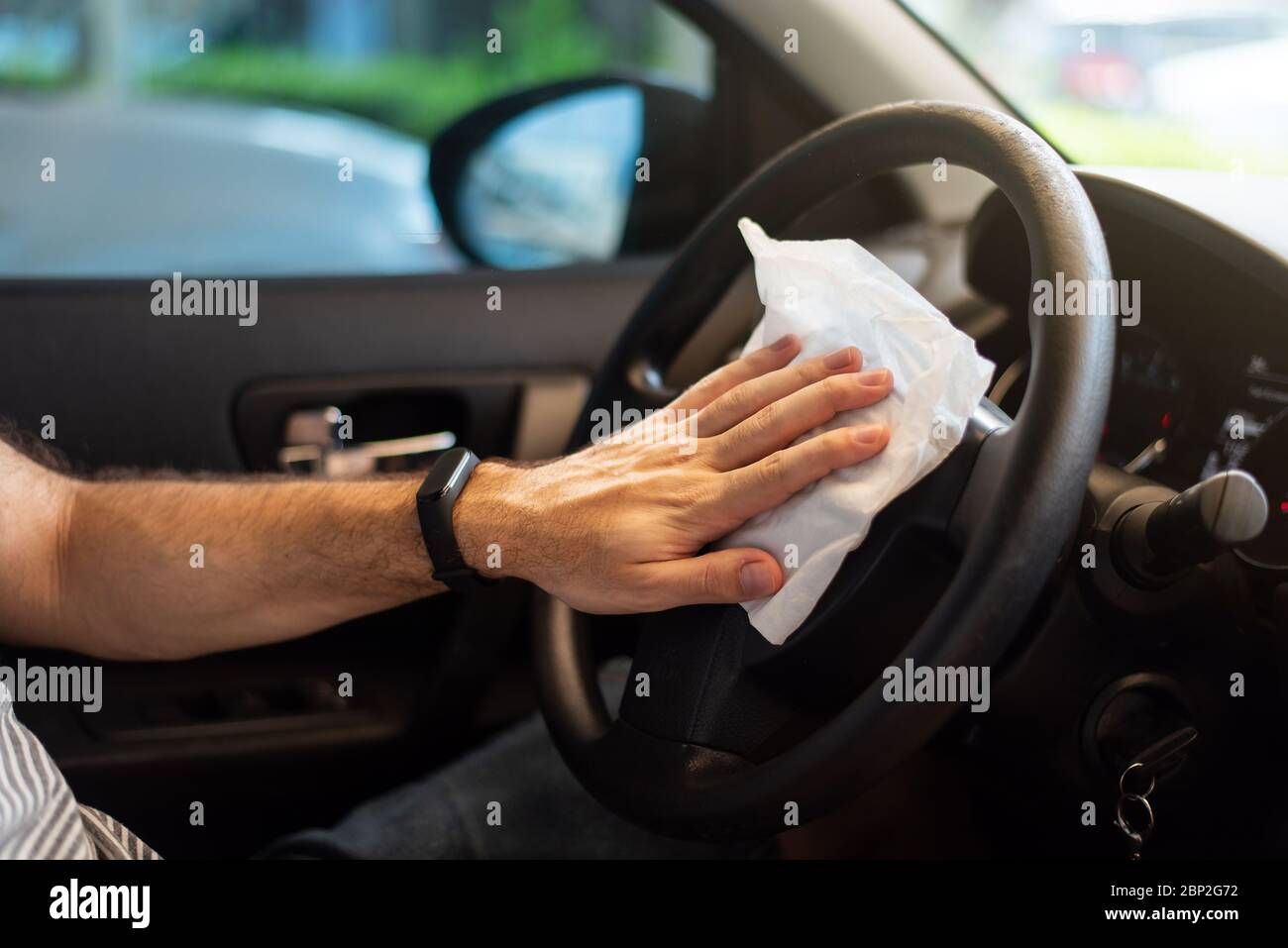Man cleaning his car steering wheel for disinfection and a safe ride during the virus pandemic closeup Stock Photo