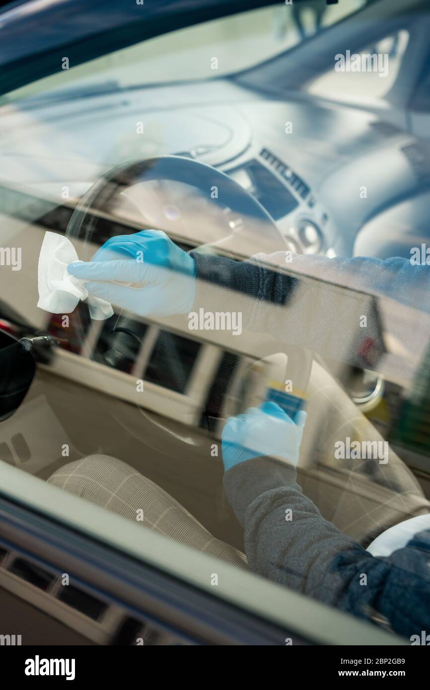 Gloved young man sitting inside car by steer and cleaning it with wet