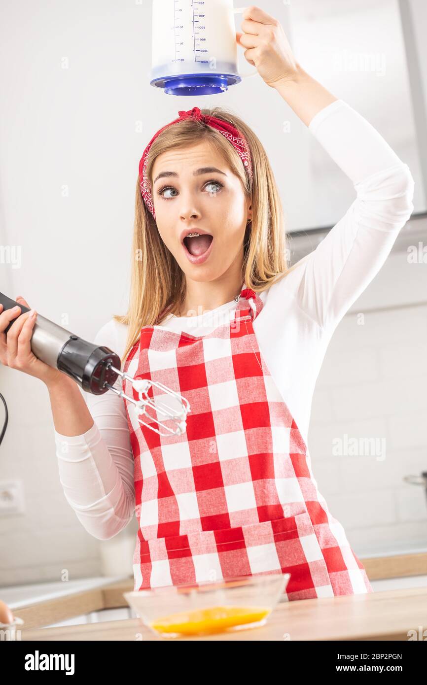 Pretty girl with surprised face expression holds hand whisk in one hand, while holding whisked