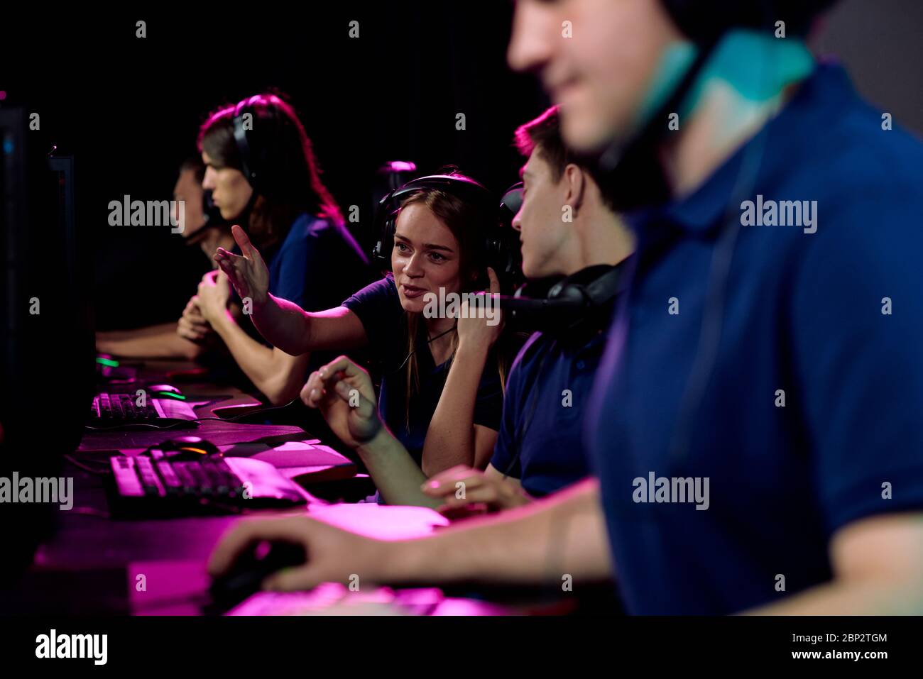 Happy girl pointing at computer screen of her friend while giving advice about network game during preparation for competition Stock Photo