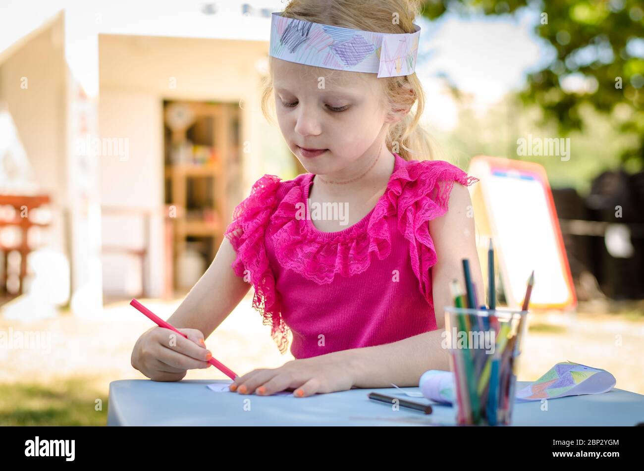 cute girl sitting outdoors behing the table coloring with pencils Stock ...