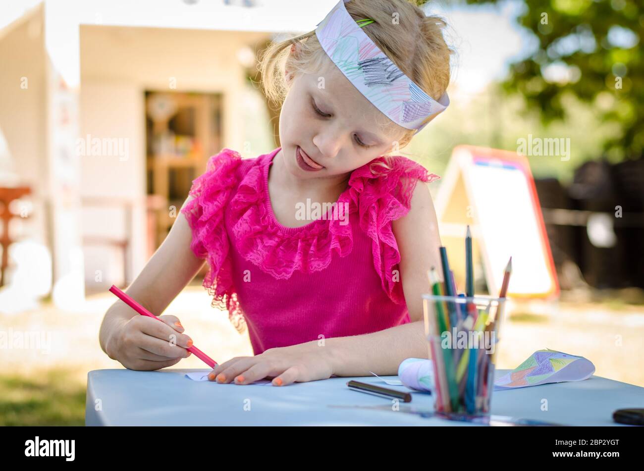 cute girl sitting outdoors behing the table coloring with pencils Stock ...