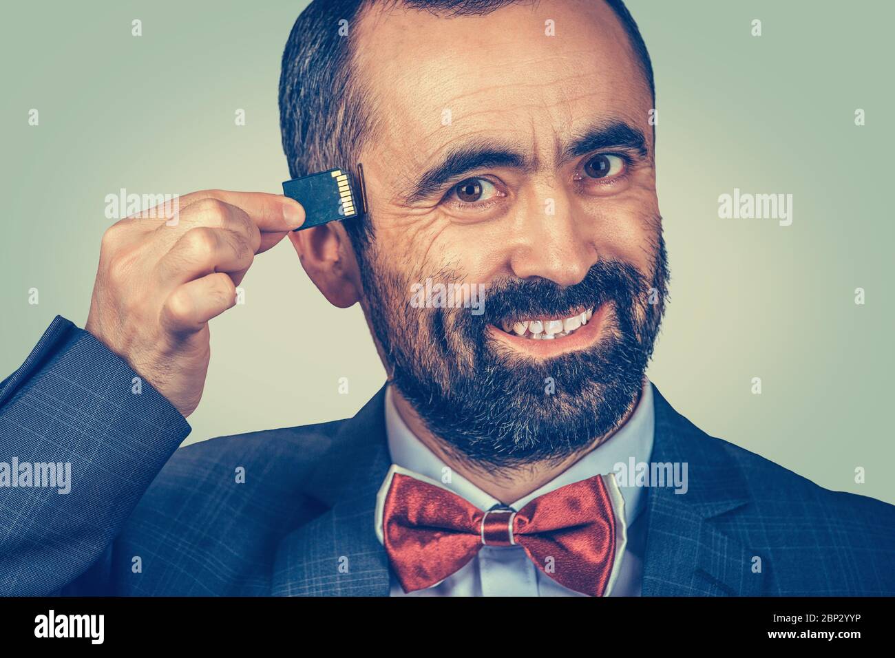 External memory needed concept. Portrait of smiling bearded businessman wearing elegant jacket and red bow tie holding Micro SD card near his head iso Stock Photo