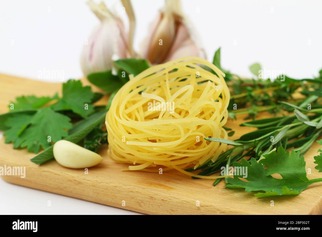 Closeup of uncooked tagliatelle, fresh herbs and garlic on wooden surface Stock Photo