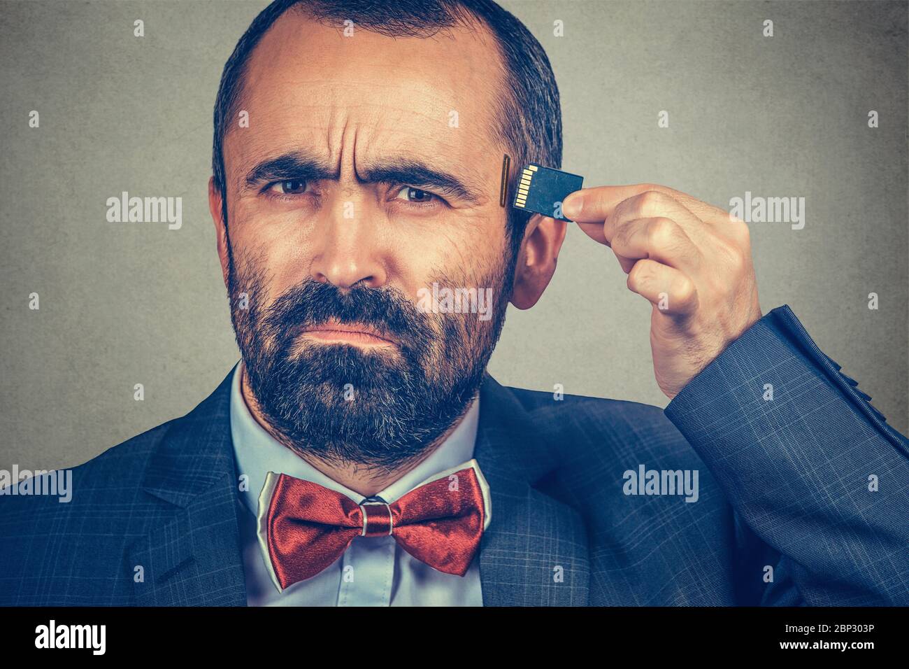 External memory needed concept. Portrait of interested bearded businessman wearing elegant jacket, red bow tie holding Micro SD card near head isolate Stock Photo