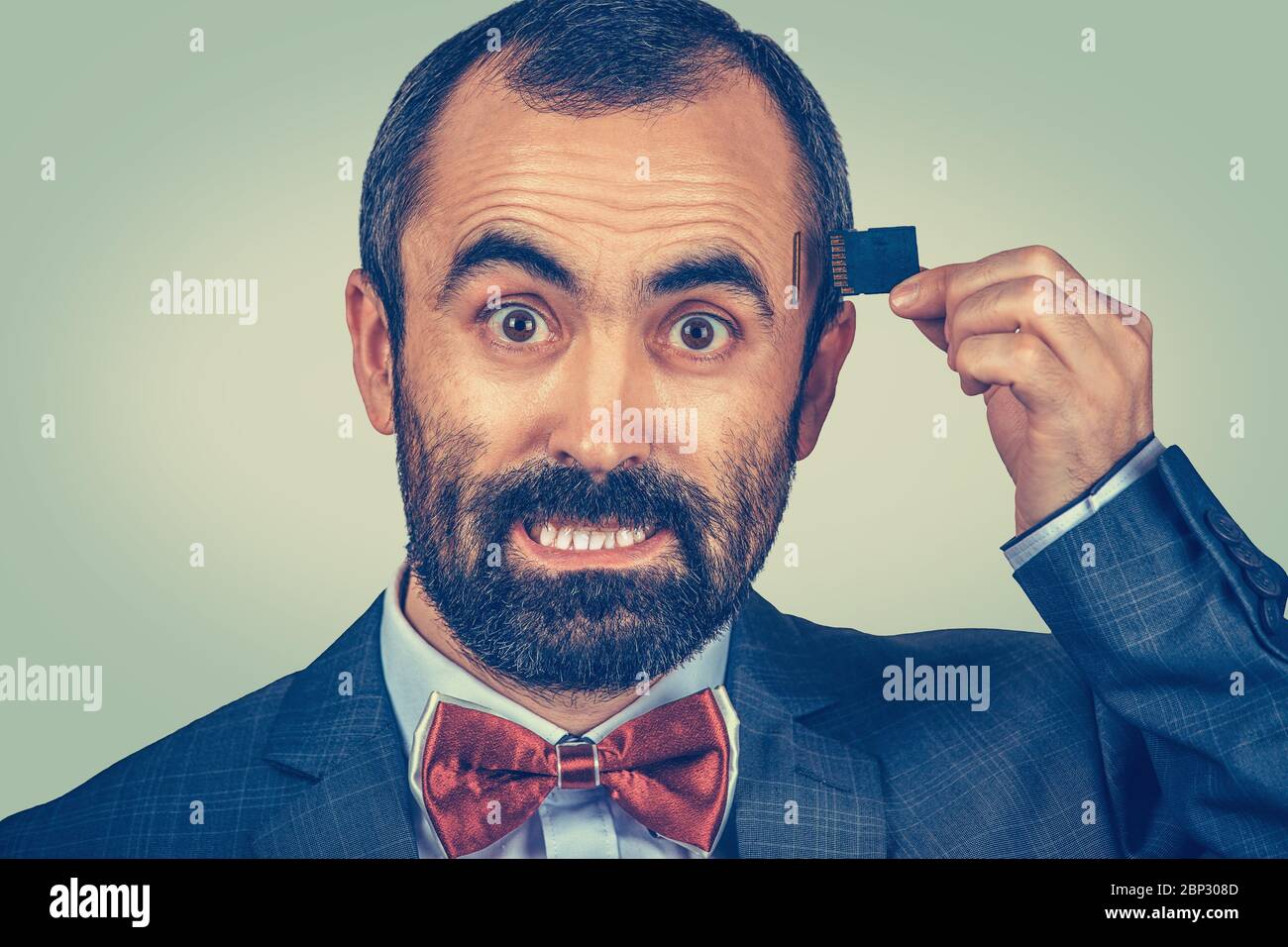 External memory needed concept. Portrait of angry bearded businessman wearing elegant jacket and red bow tie holding Micro SD card near his head isola Stock Photo