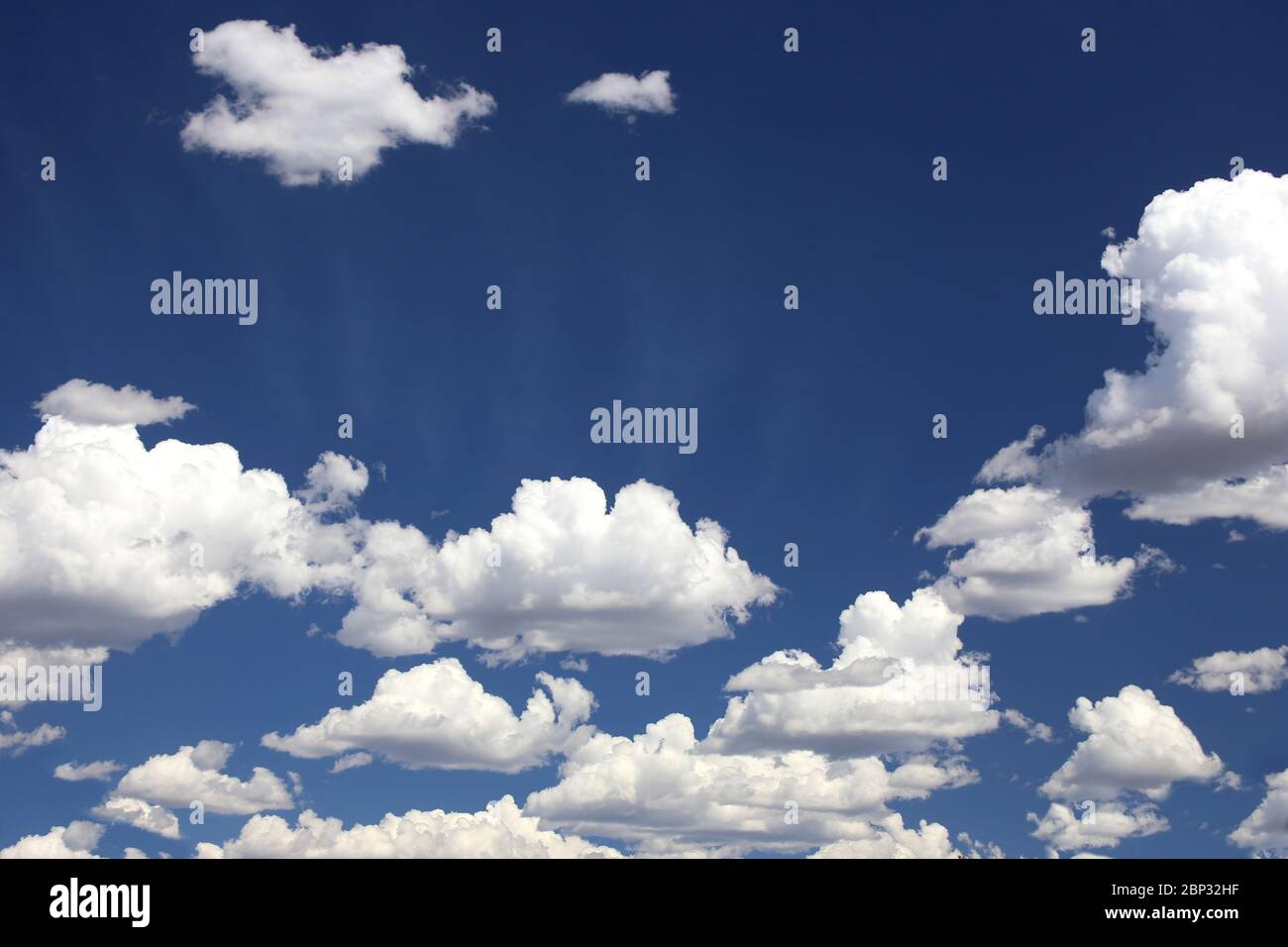 Puffy cumulus clouds set against a deep blue sky with subtle sun rays Stock Photo