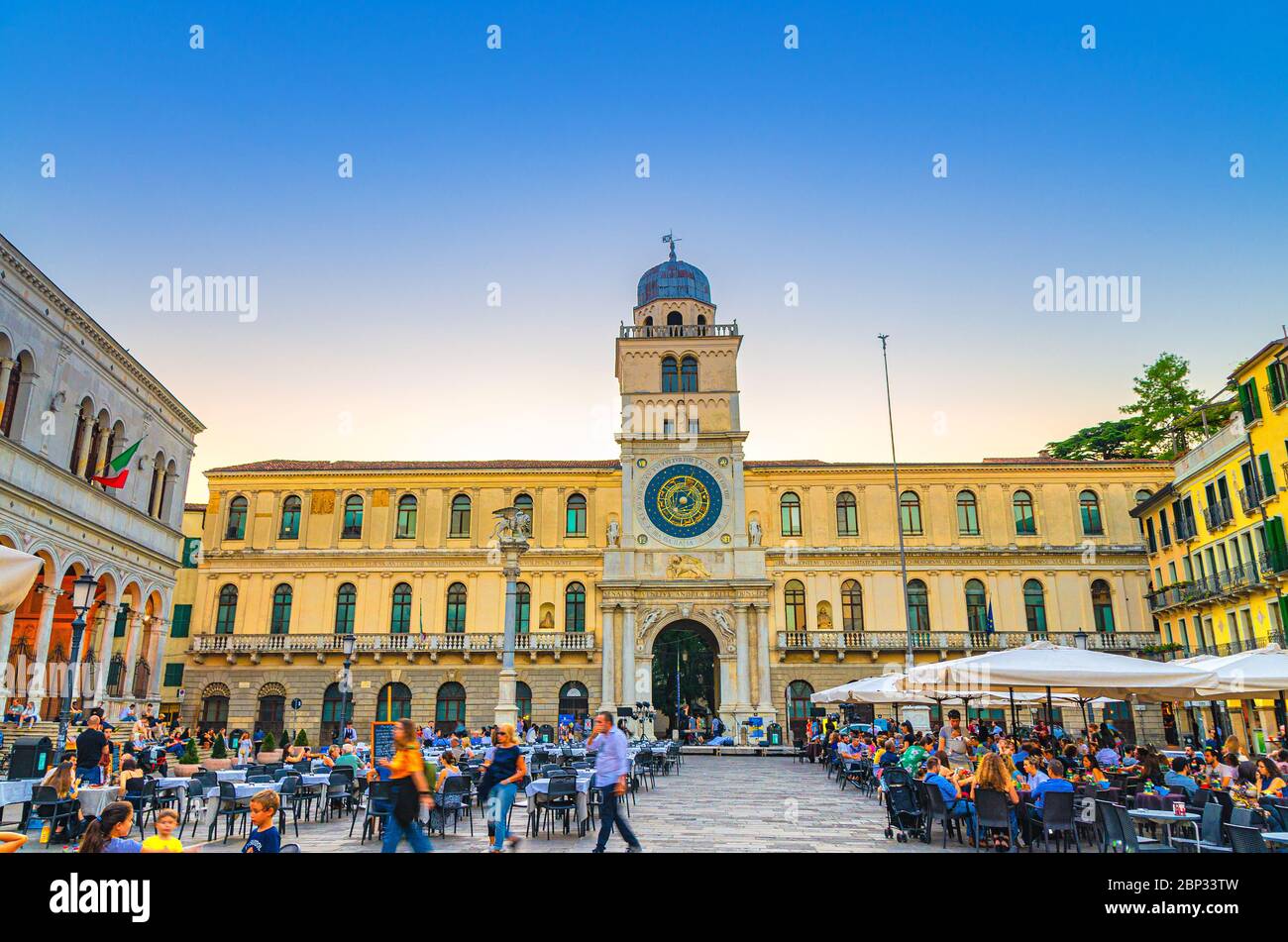 Padua, Italy, September 12, 2019: Torre dell'Orologio clock tower with astronomical clock and restaurant tables in the Piazza Plaza Dei Signori square, twilight evening view, Veneto Region Stock Photo