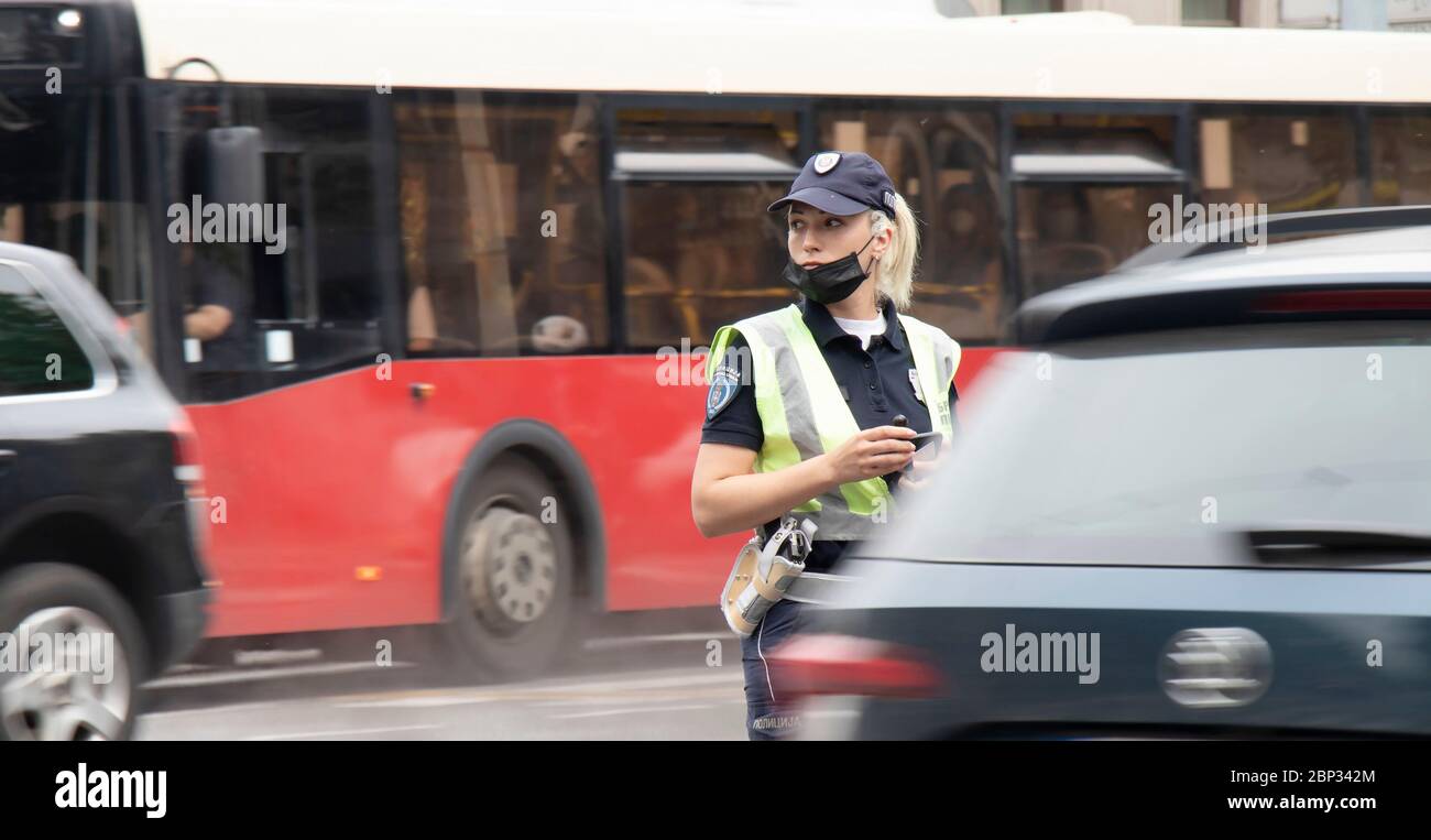 Belgrade, Serbia - May 15, 2020: Traffic policewoman on duty, standing in the intersection while vehicles moving past in motion blur Stock Photo