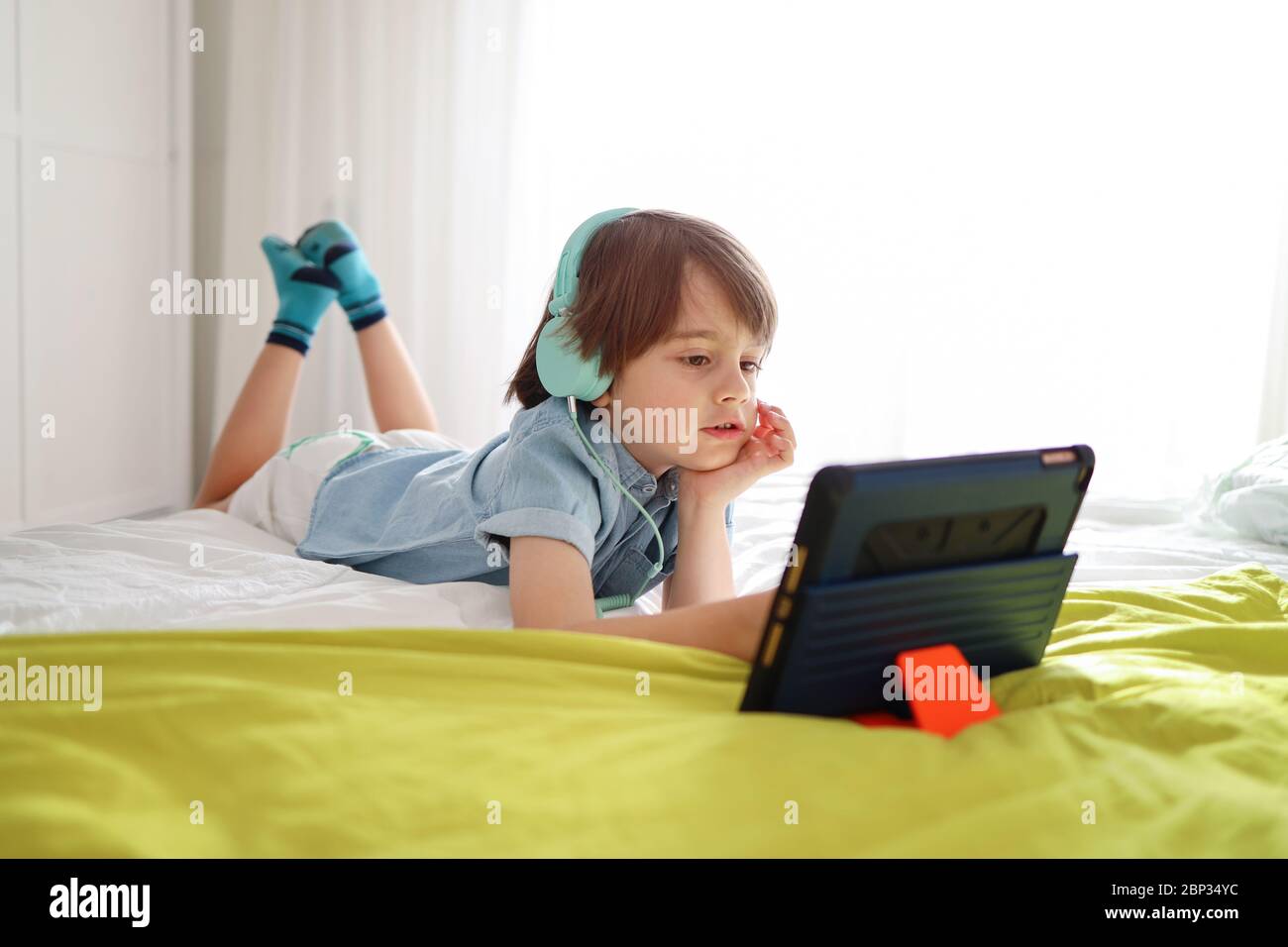Relaxed little boy doing online lesson from home using headphones and a tablet. Social distance during Quarantine and Online Education Concept Stock Photo