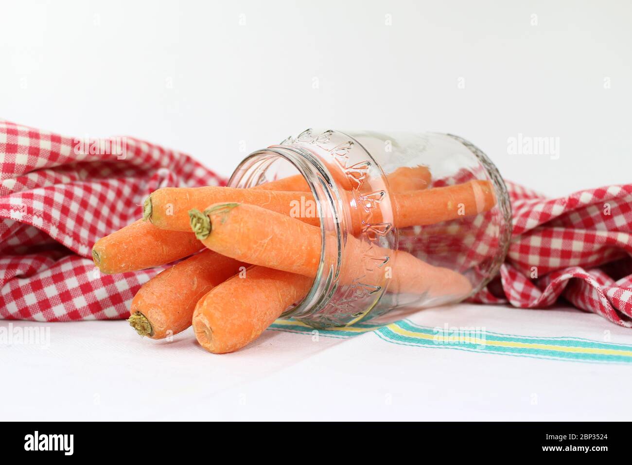 Carrots in the glass jar, with the red and white checkered tablecloth and a cotton towel with a colored printed line. Stock Photo