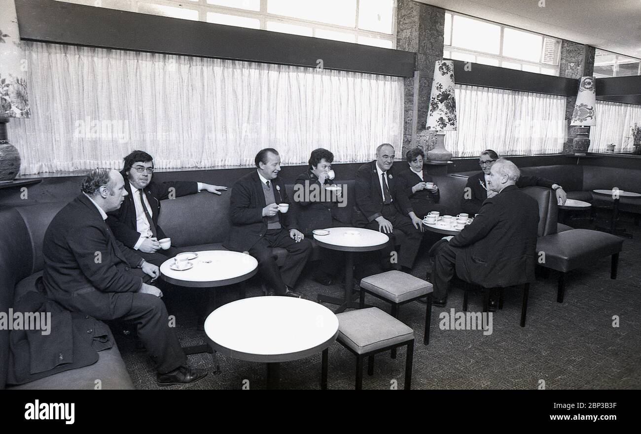 Interior picture showing uniformed bus workers sitting together in a rest room at New Cross bus depot, south east London, England, 1974. The bus crew are having a break, a cup of tea, a smoke and a chat with work colleagues. Orginally a tram depot, New Cross was converted into a bus depoet n 1952 and was one of the largest of London's bus garages. Stock Photo