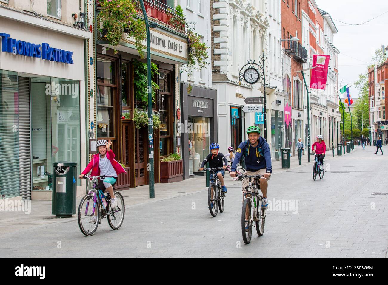 Family cycling through deserted Grafton Street in Dublin Ireland as businesses and shops remain closed and footfall plummets due to Covid-19 lockdown Stock Photo