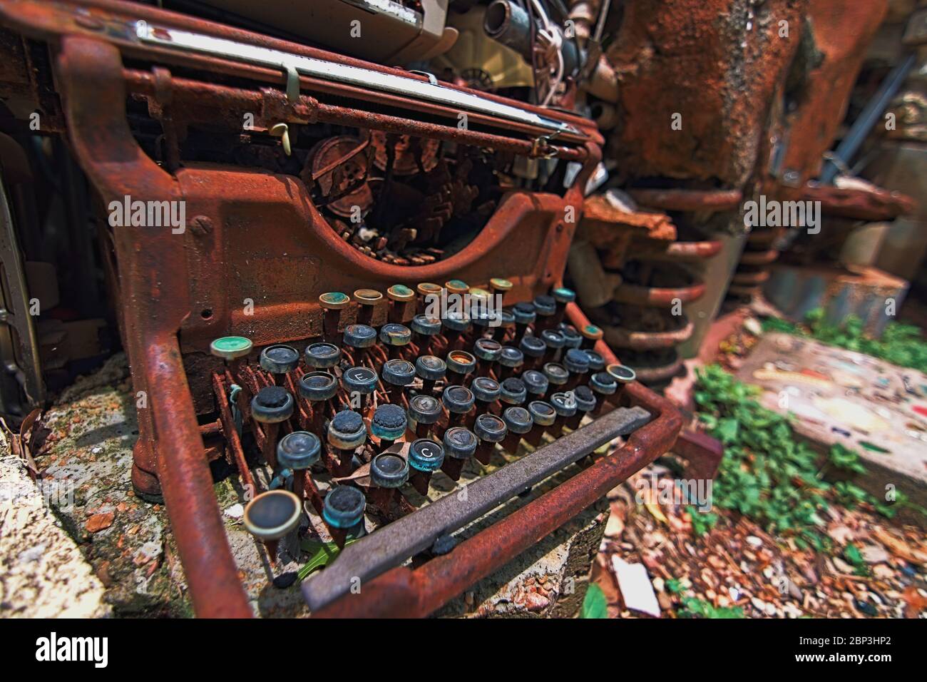 Classic rusty typewriter sits broken and discarded on ground exposed to elements a relic of previous times. Part of an art installation Cathedral of J Stock Photo