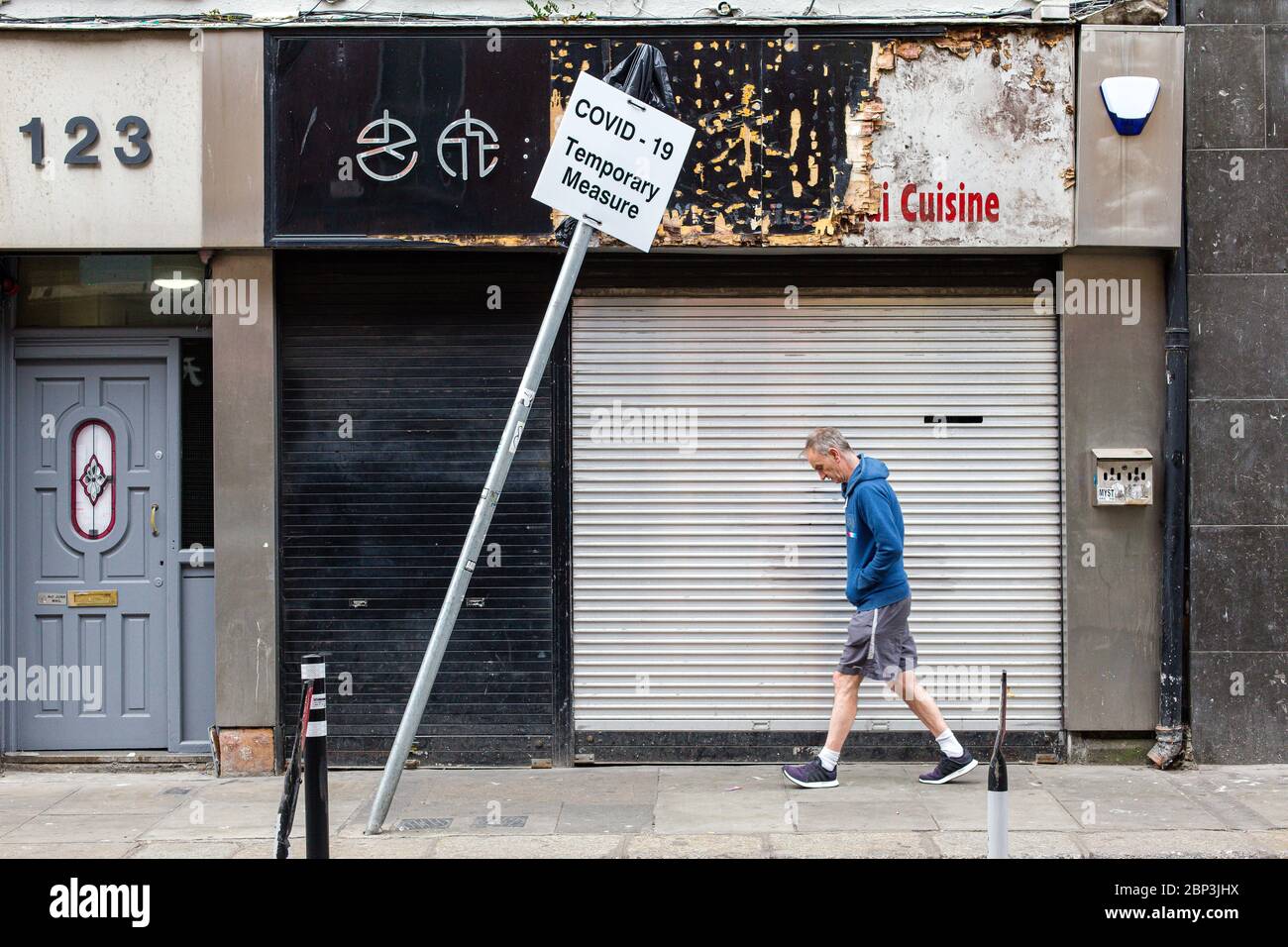 Man passes by closed down shop and leaning sign - Covid-19 Temporary Measure. Coronavirus pandemic and its economic impact. May 2020, Dublin, Ireland. Stock Photo