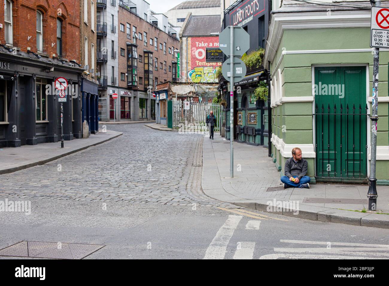 Dublin, Ireland. May 2020. Man sitting on the pavement on the deserted Parliament Street in Dublin. Covid-19 pandemic restrictions during lockdown. Stock Photo