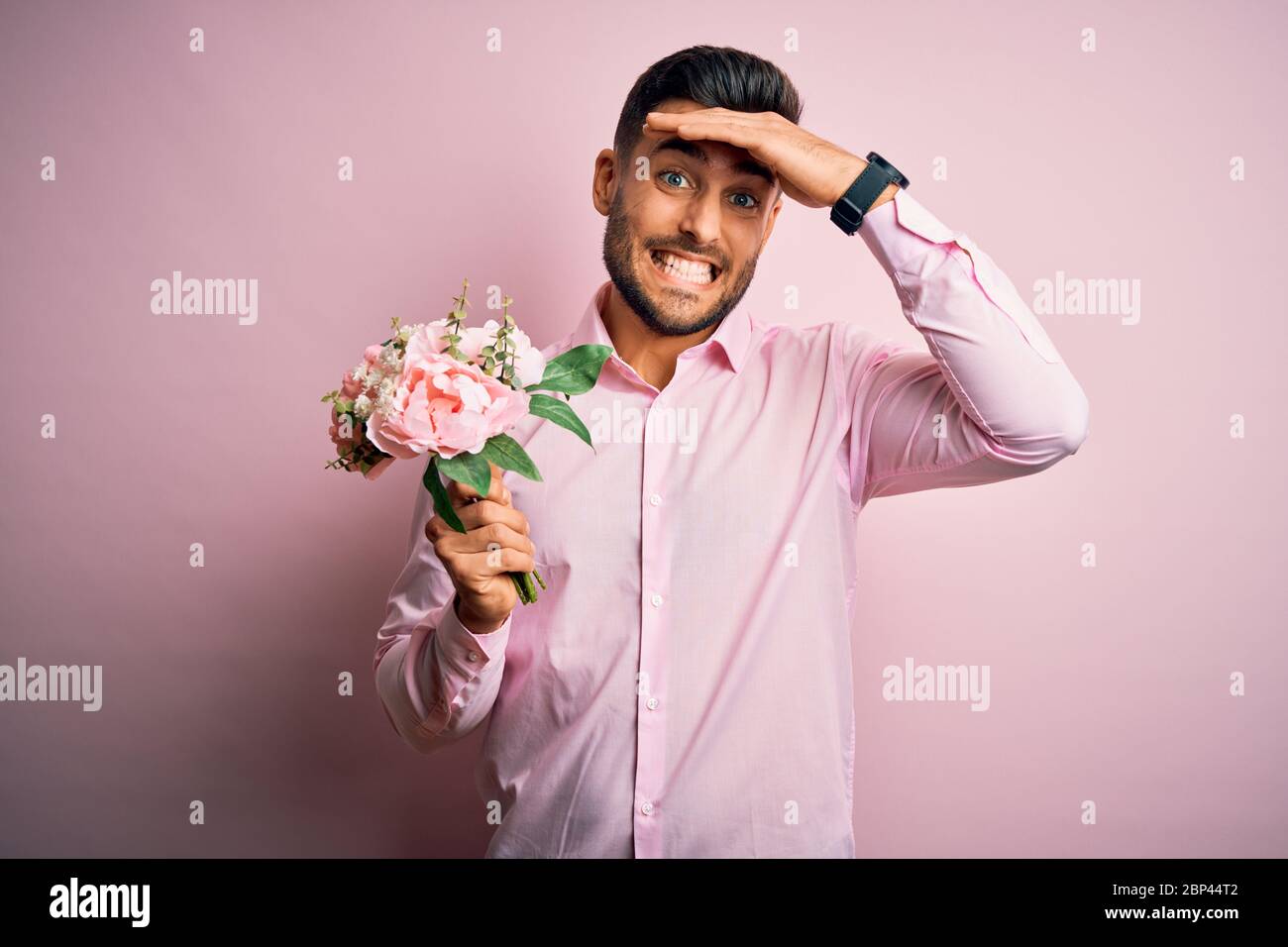 Young romatic man holding bouquet of spring flowers over pink isolatd ...