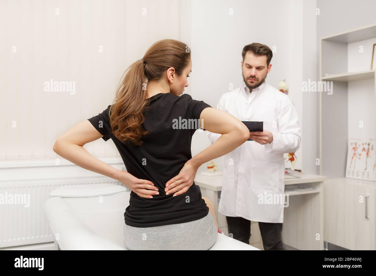 Male doctor examining female patient suffering from back pain. Medical