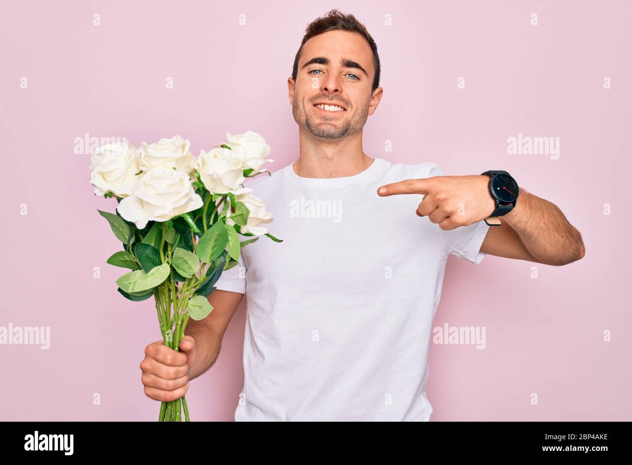 Young handsome man with blue eyes holding bouquet of flowers over pink ...