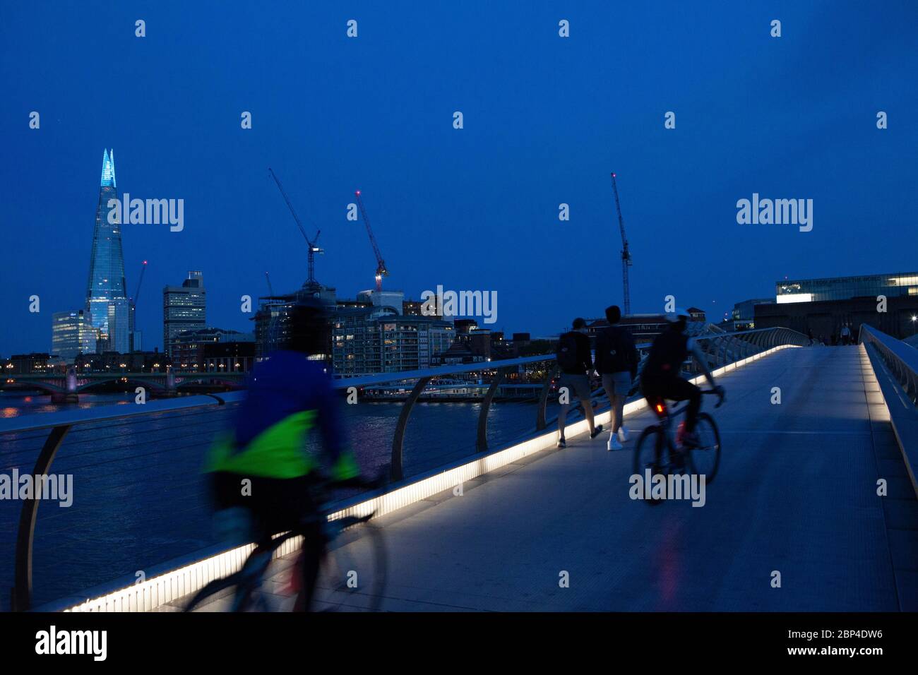 London, UK, 17 May 2020: People walk and cycle across the Milemmium Bridge as the top of the Shard is illuminated blue and Tate Modern carries signage saying 'Thank you key workers' to honour NHS staff and other care workers and frontline key workers. Anna Watson/Alamy Live News Stock Photo