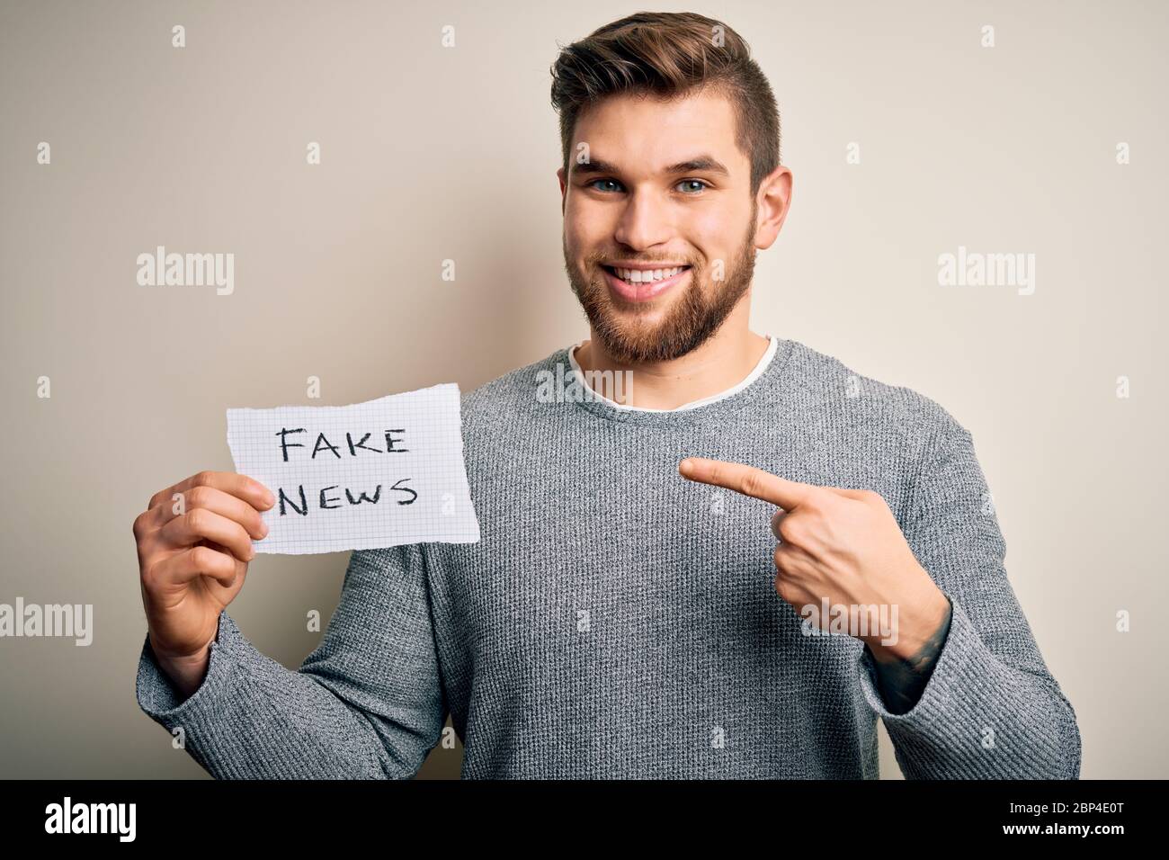 Young blond man with beard and blue eyes holding paper with fake news ...
