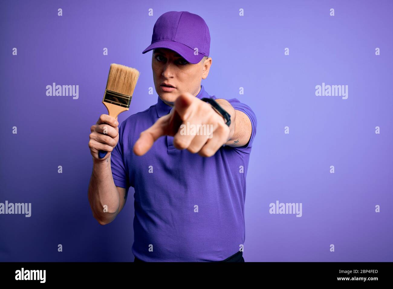 Young modern decorator painter man holding paint brush over purple ...