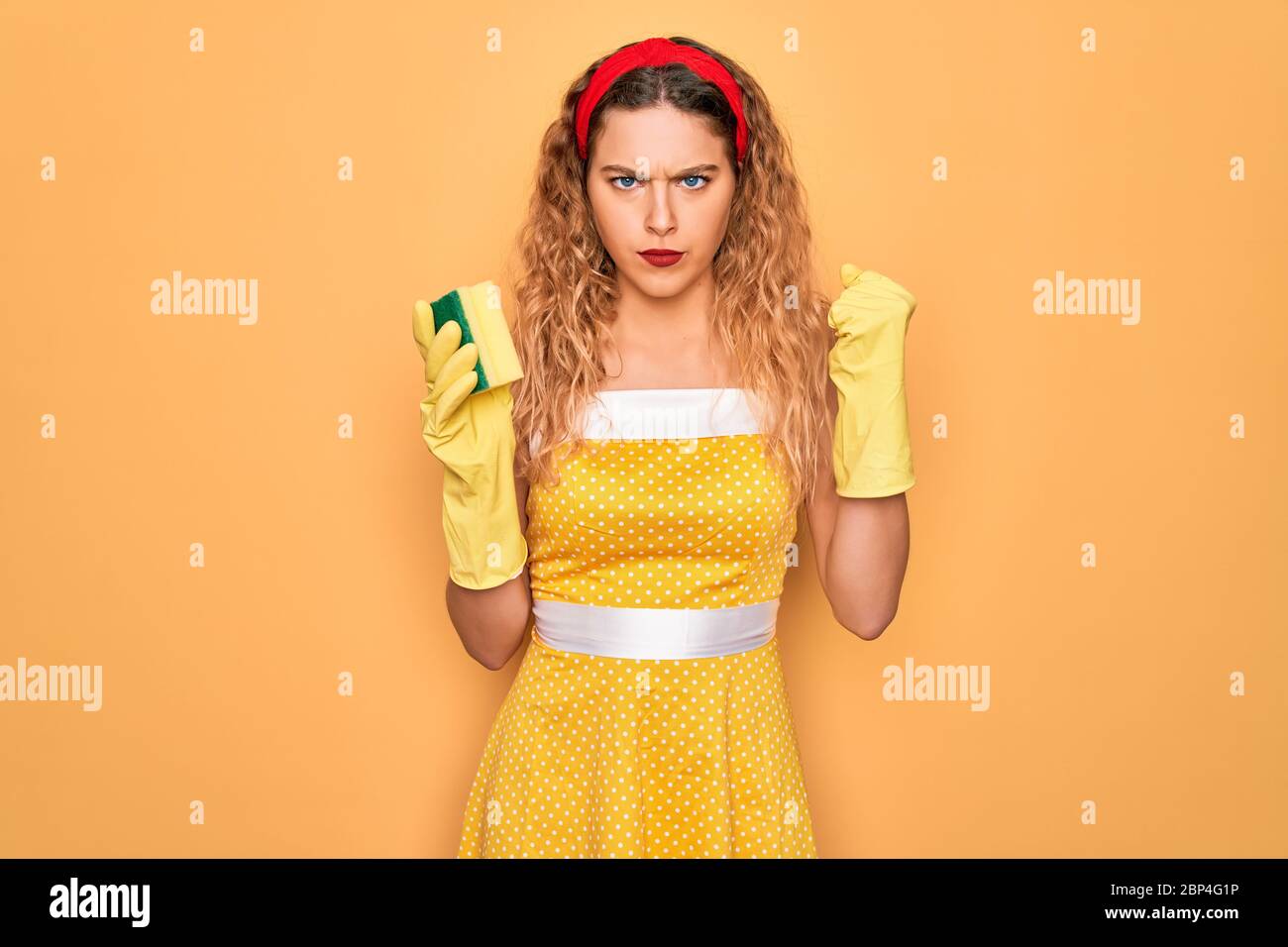 Young beautiful blonde woman with blue eyes cleaning using gloves and cleaner scourer annoyed and frustrated shouting with anger, crazy and yelling wi Stock Photo