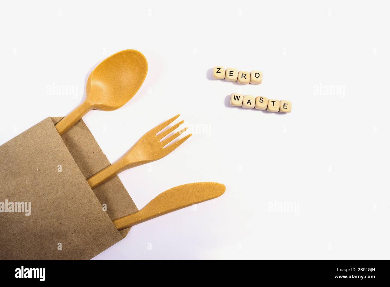 Eco knife, fork and spoon food made of natural eco recycle reusable material in the carton craft envelope, and the sign zero waste on wooden bricks is Stock Photo