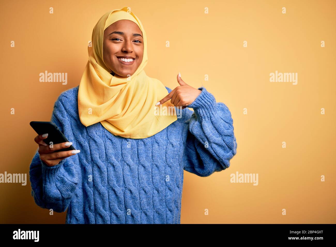 Young African American afro woman wearing muslim hijab using smartphone ...