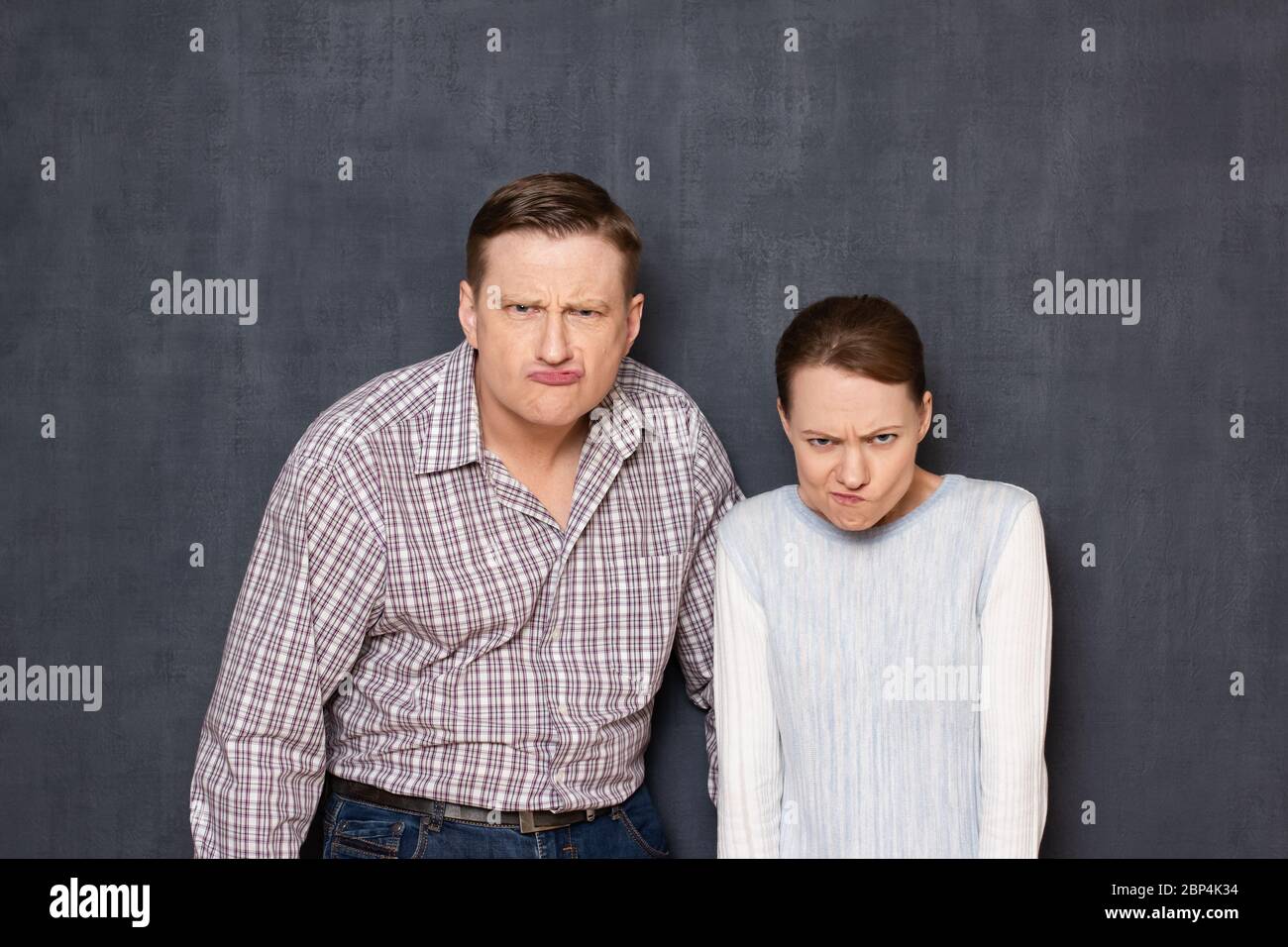Studio waist-up portrait of funny caucasian young adult couple grimacing and making stupid angry faces, looking with dissatisfied expression from unde Stock Photo