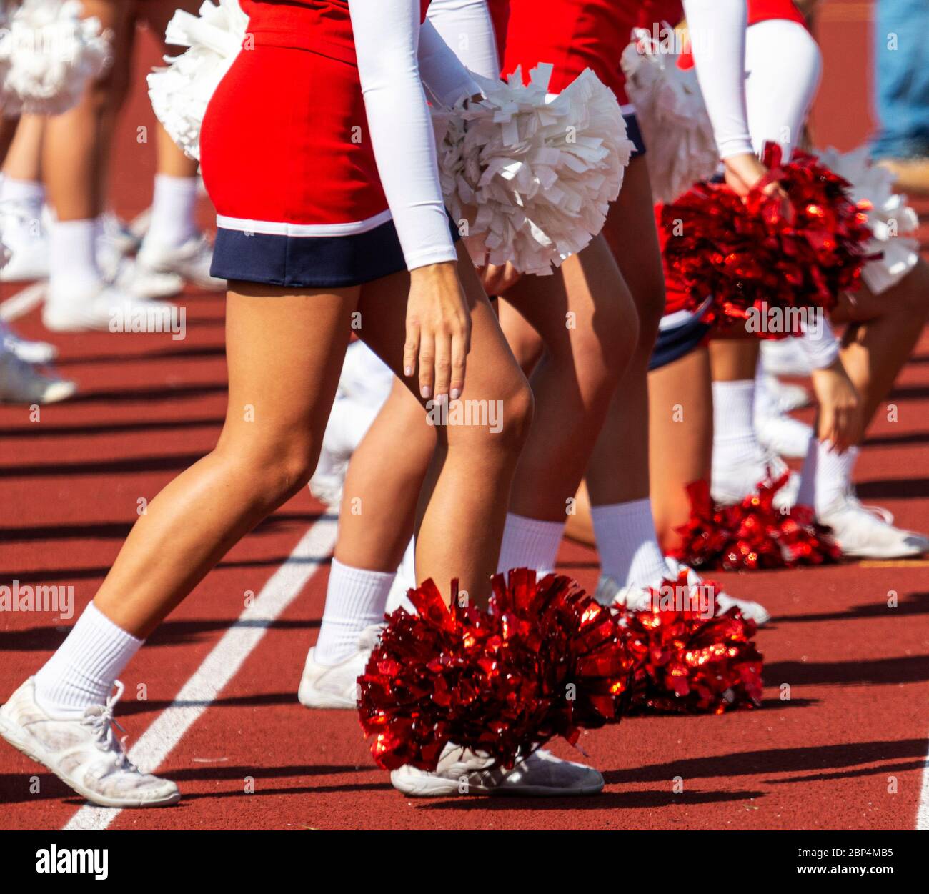 A high shcool cheerleader in a red white and blue uniform dropping her pom pom on to the track after performing. Stock Photo