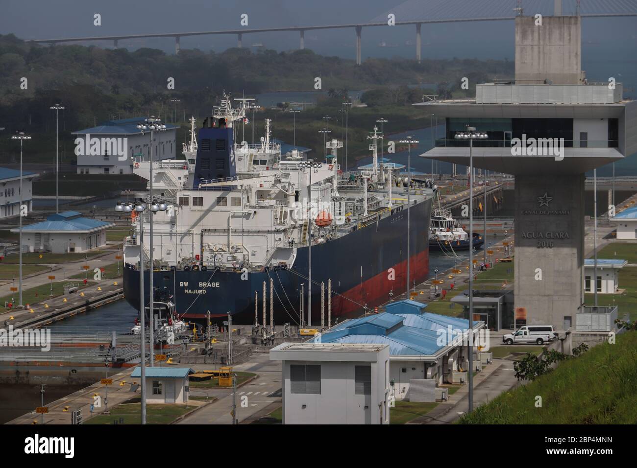 Large ship passing control tower at the Agua Clara lock, from Lake Gatun to the Atlantic entrance to the Panama Canal. Atlantic Bridge in distance. Stock Photo