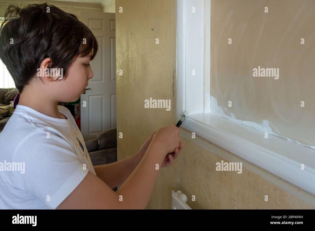 A young child helps to paint some woodwork with gloss paint as part of a family DIY project. Stock Photo