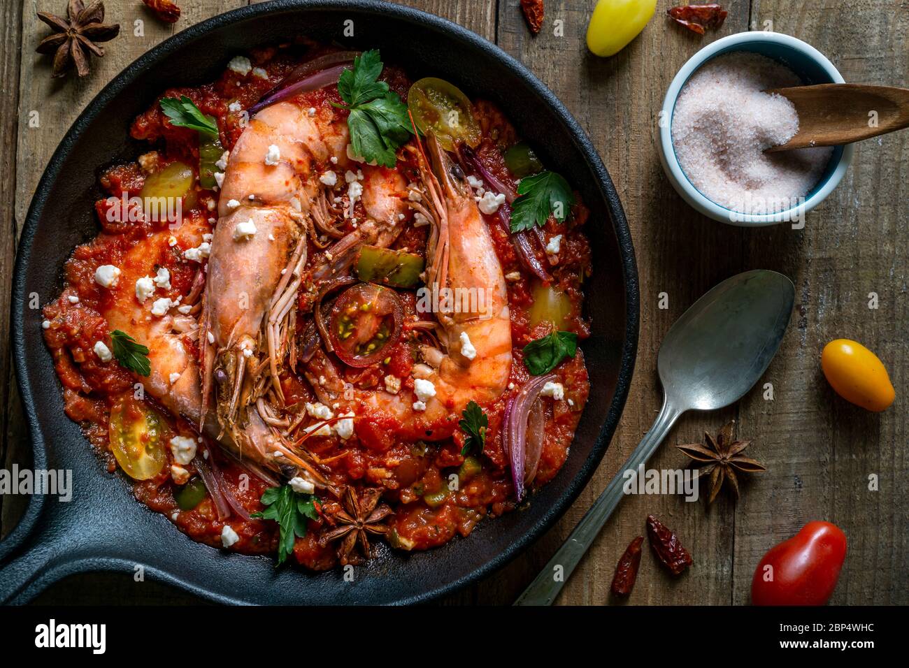Prawns cooked in cast iron pan with red tomato sauce with parsley and feta cheese. Stock Photo