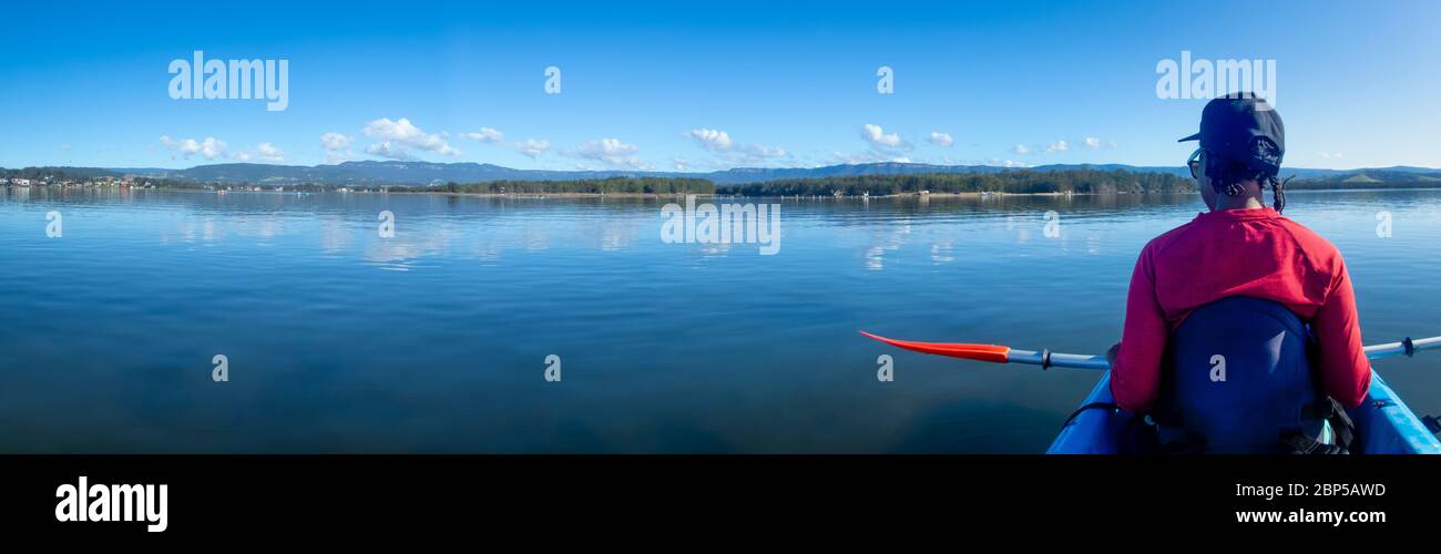 African Australian woman kayaking on calm peaceful lake in morning sunshine, Australia Stock Photo