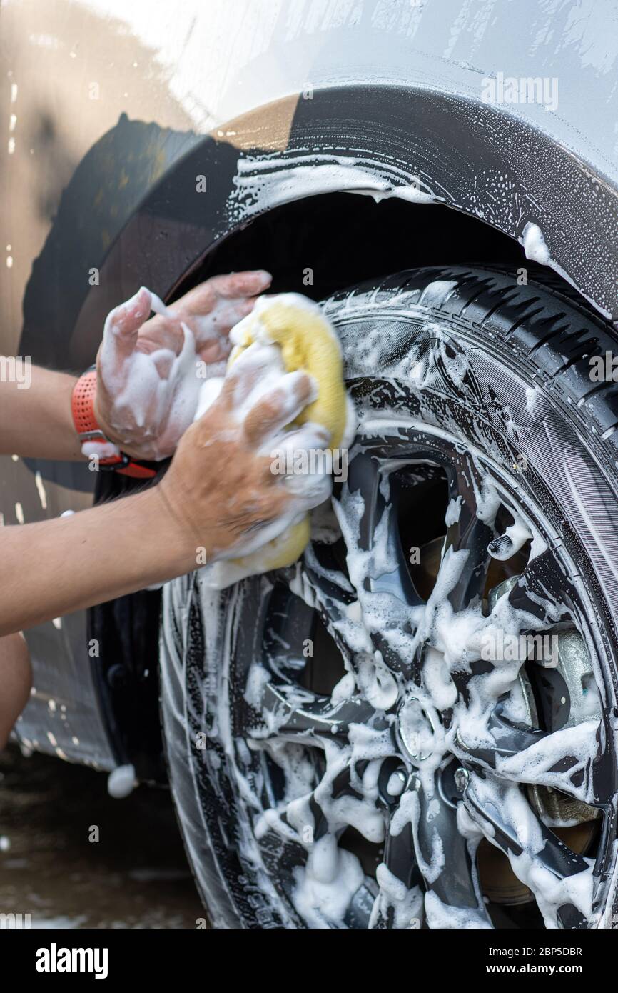 Hand washing wheel of car with soapy water. Man cleans car with sponge