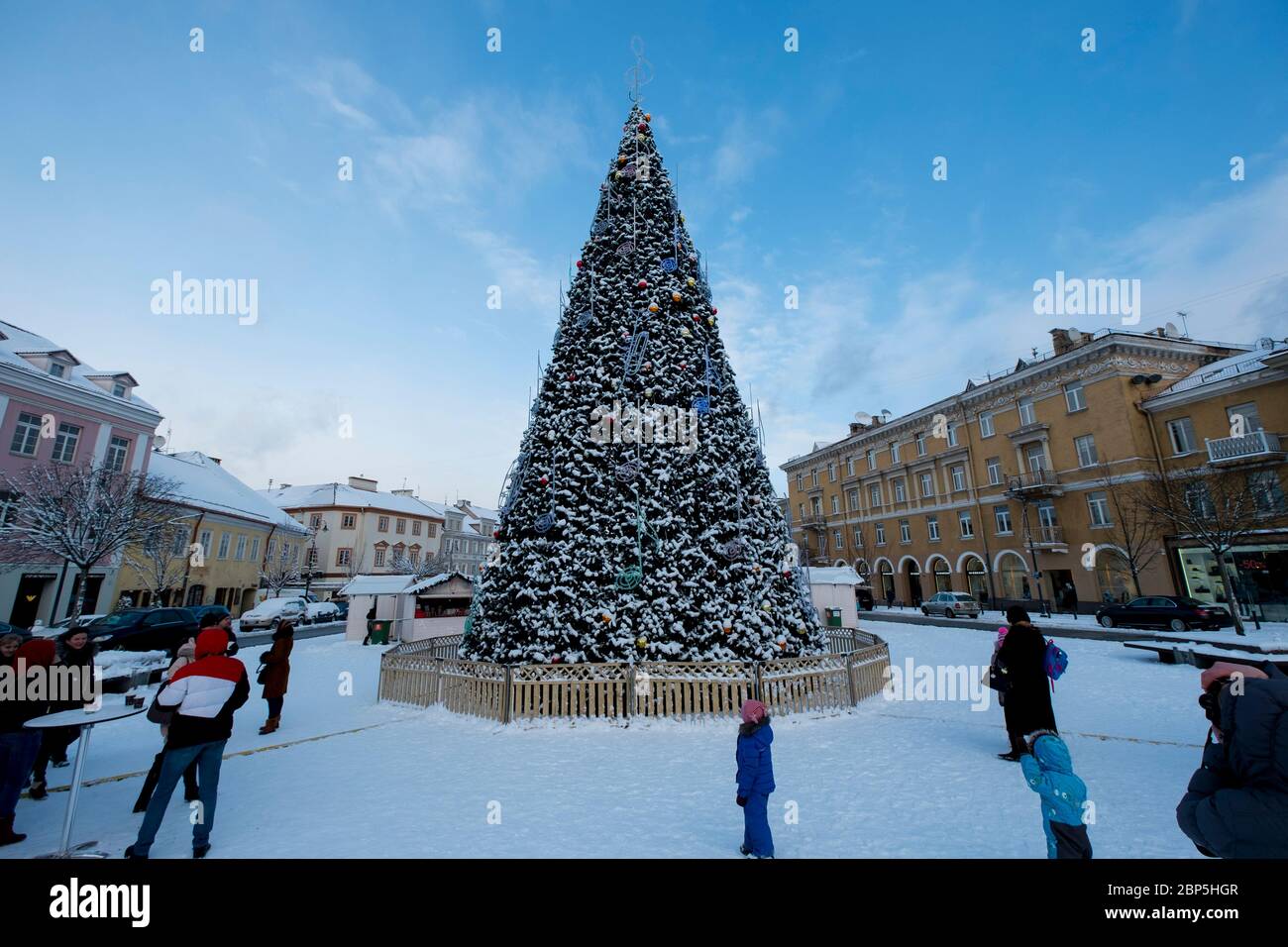 Tourists enjoying the big, decorated Christmas tree in the Rotušė square on a winter's day in Old Town. In Vilnius, Lithuania. Stock Photo