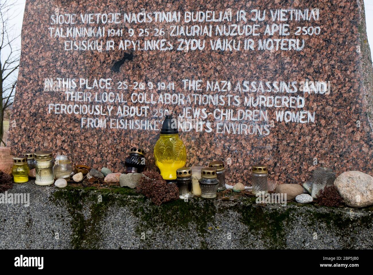 Candles and stones on the brown granite marker, commemorating the place where all the Jewish women and children from the town were executed.  In Eišiš Stock Photo