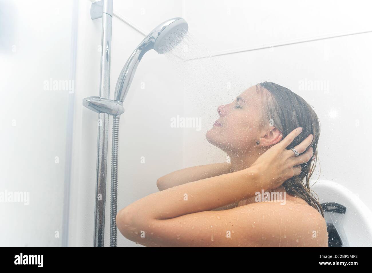 Young woman taking a hot shower showering hair relaxing under warm running ...