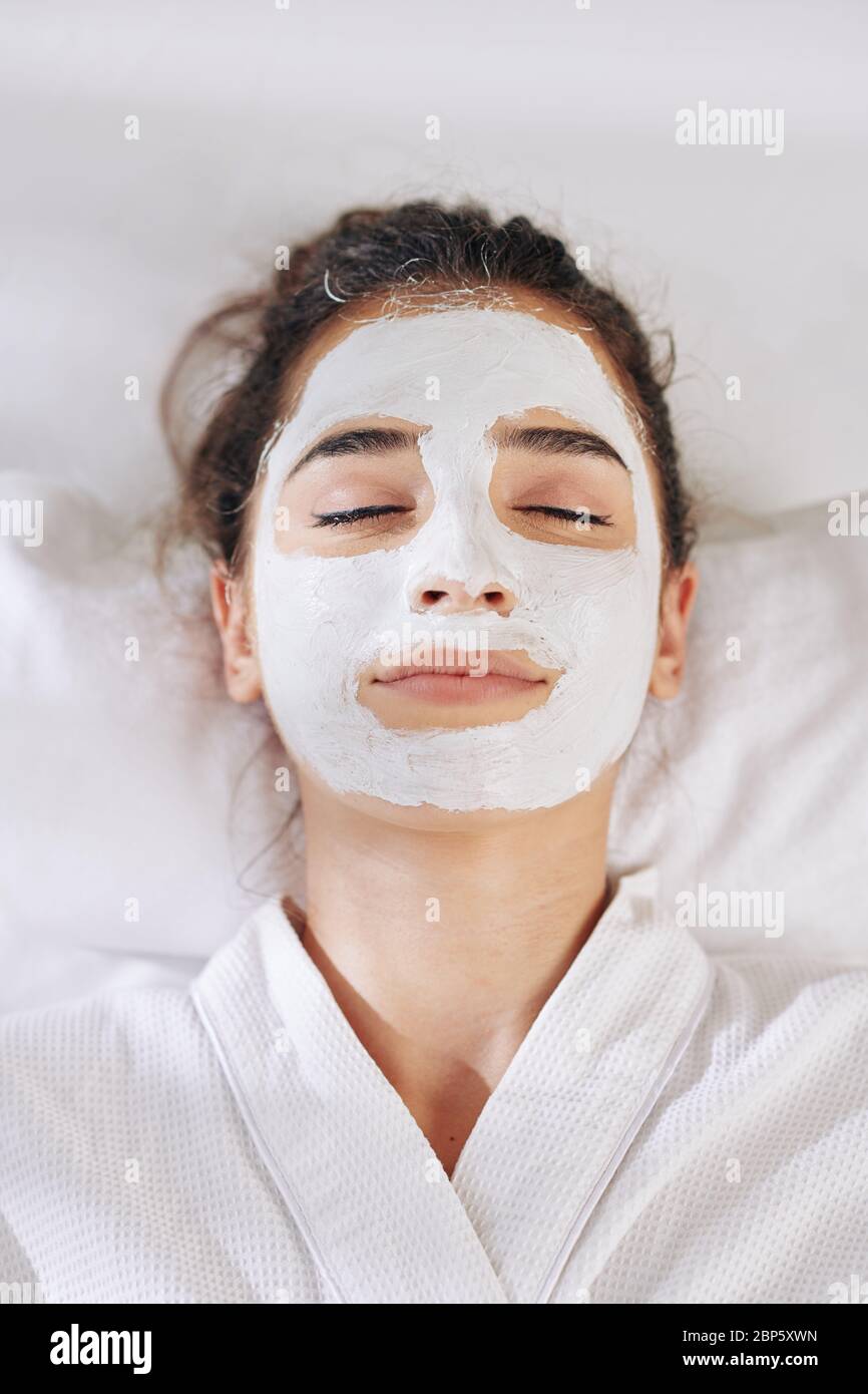 Smiling young woman resting in bad with detoxifying and brightening white clay mask Stock Photo