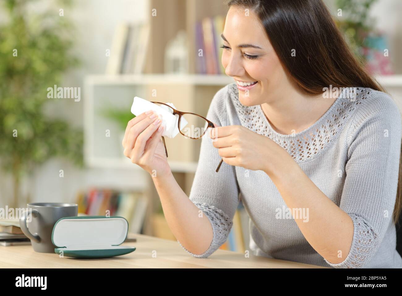 Happy woman cleaning eyeglasses with tissue paper sitting on a desk at
