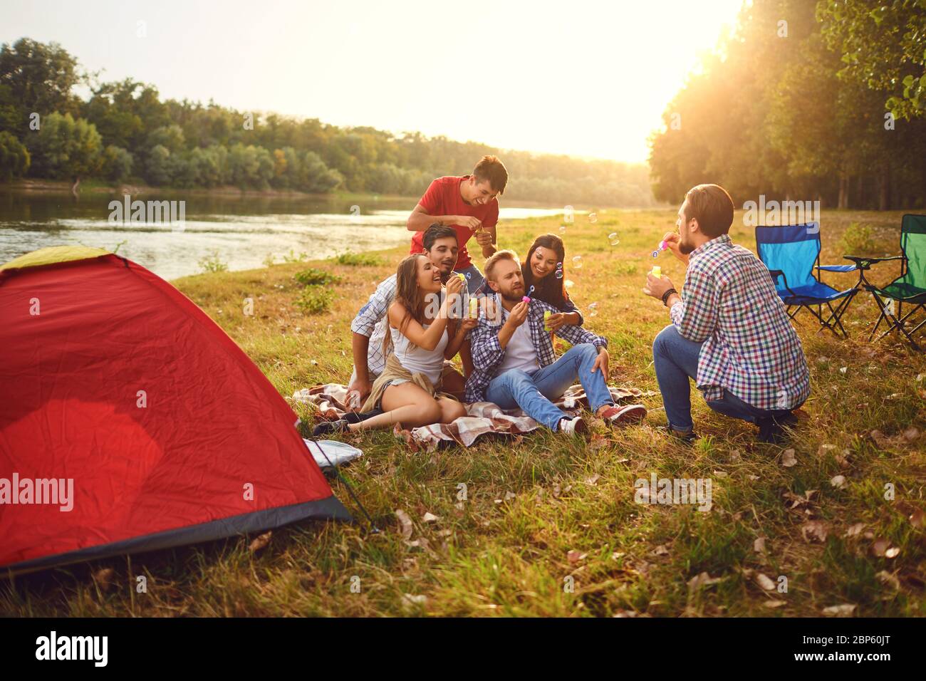 Young people make soap bubbles while sitting on the grass on in nature. Stock Photo